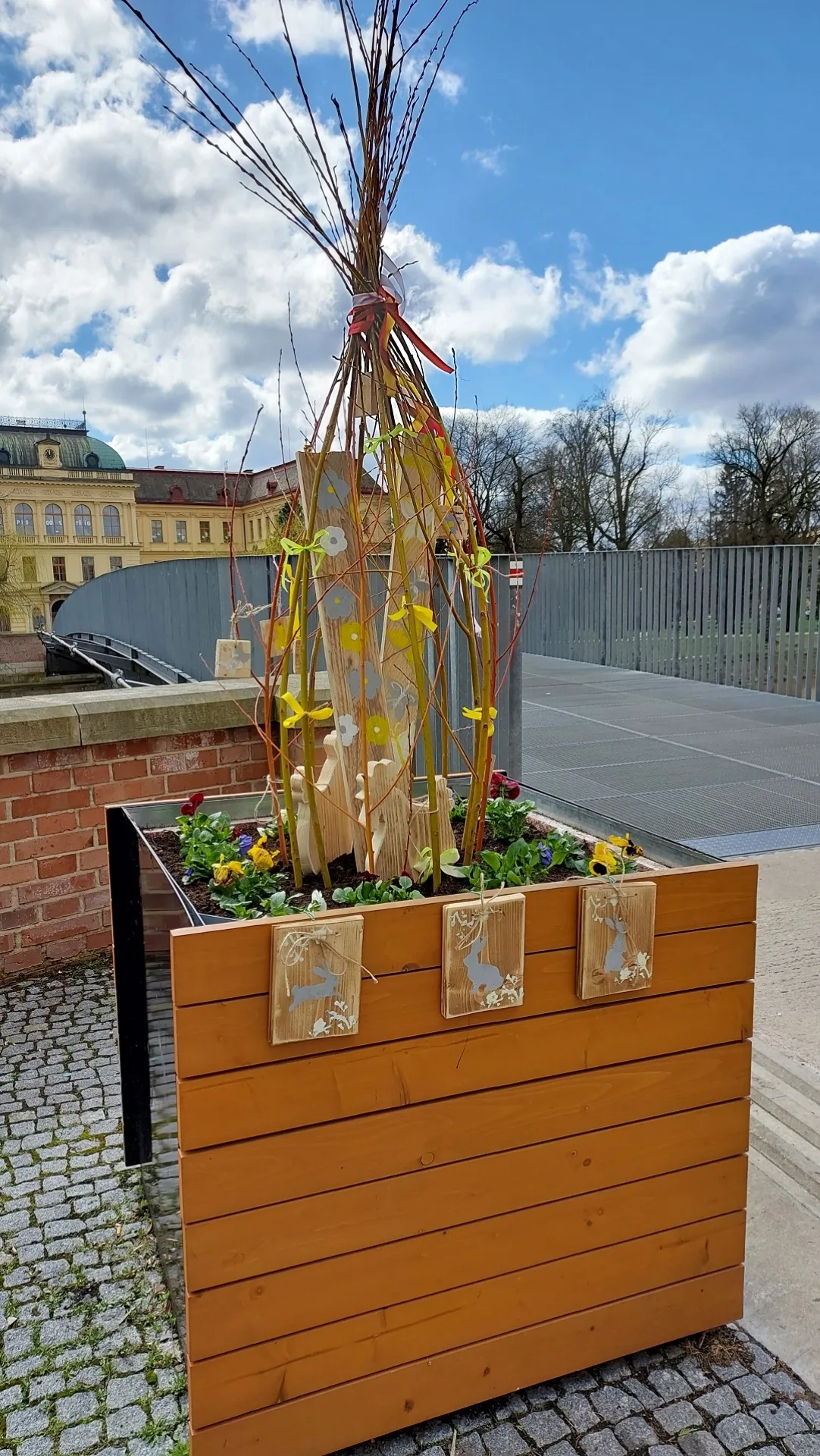 Květináč s maceškami, vrbovými proutky a výzdobou z keramických výrobků a dalšími jarními dekoracemi